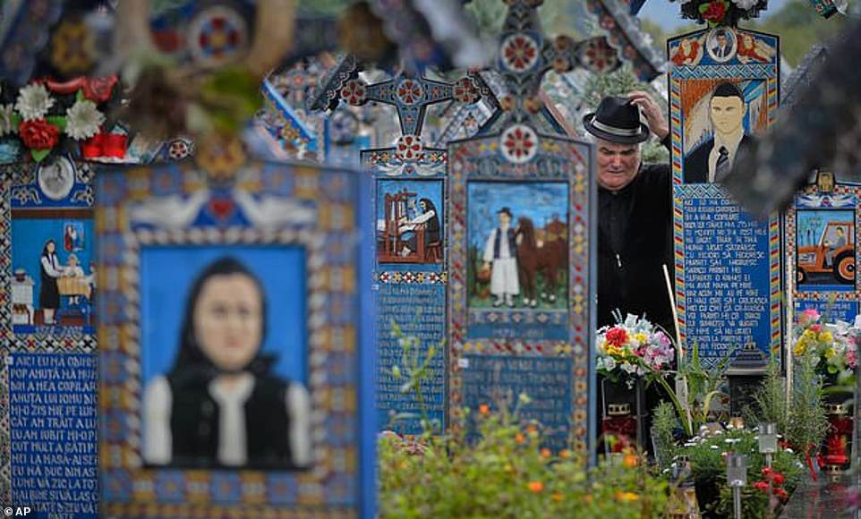 Un homme pleure sur la tombe d'un parent debout entre les croix peintes du cimetière joyeux