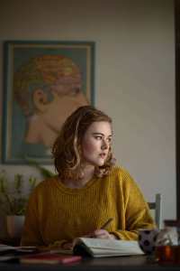L'auteur Caroline Hardaker est assise à un bureau, détournant les yeux de la caméra avec un stylo à la main